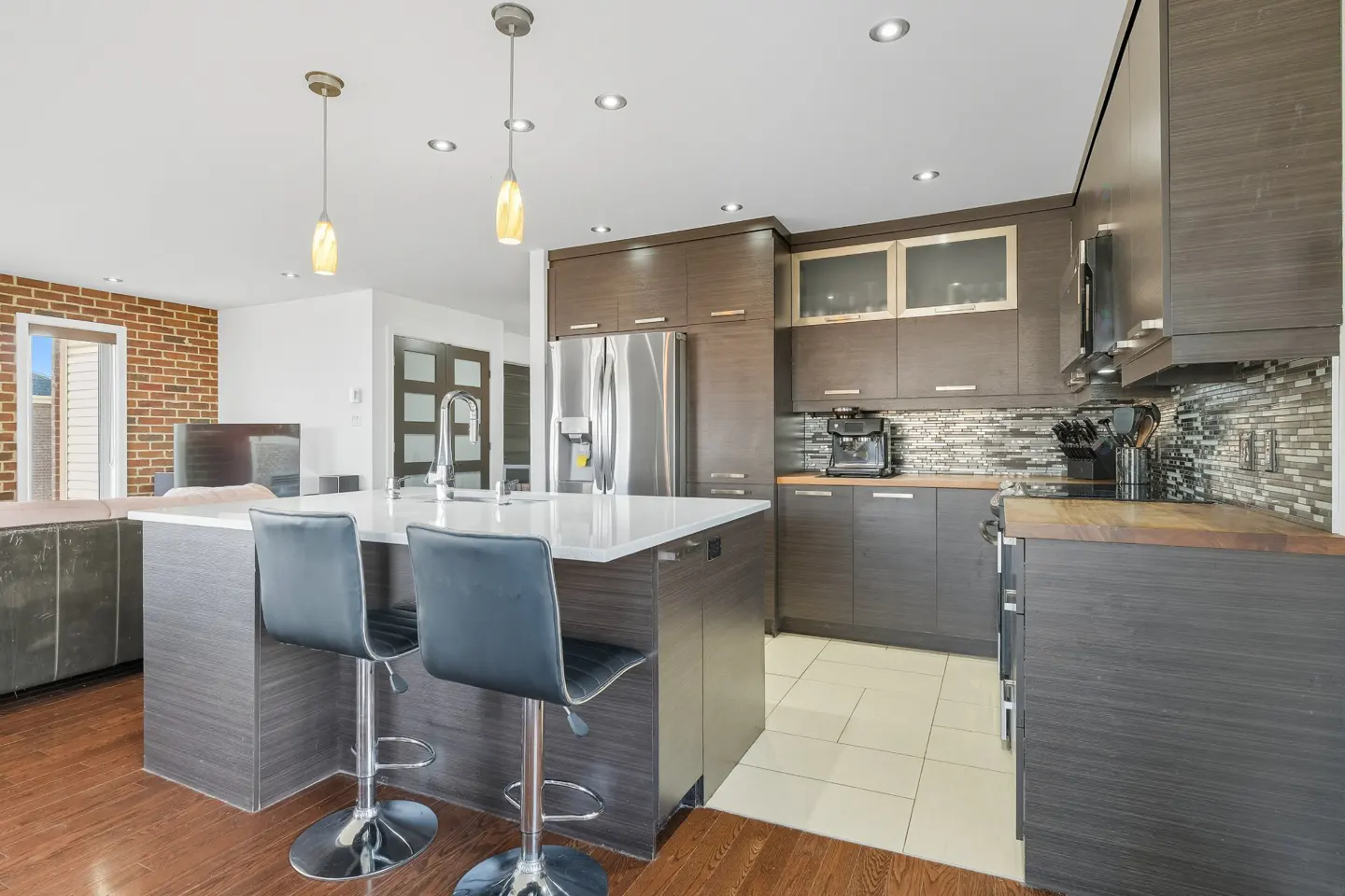 A modern kitchen with dark wood cabinets, a white countertop island with two black stools, and stainless steel appliances.