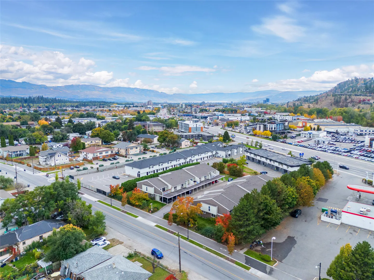 Aerial view of a neighborhood with townhouses, trees with autumn colors, and mountains in the background.