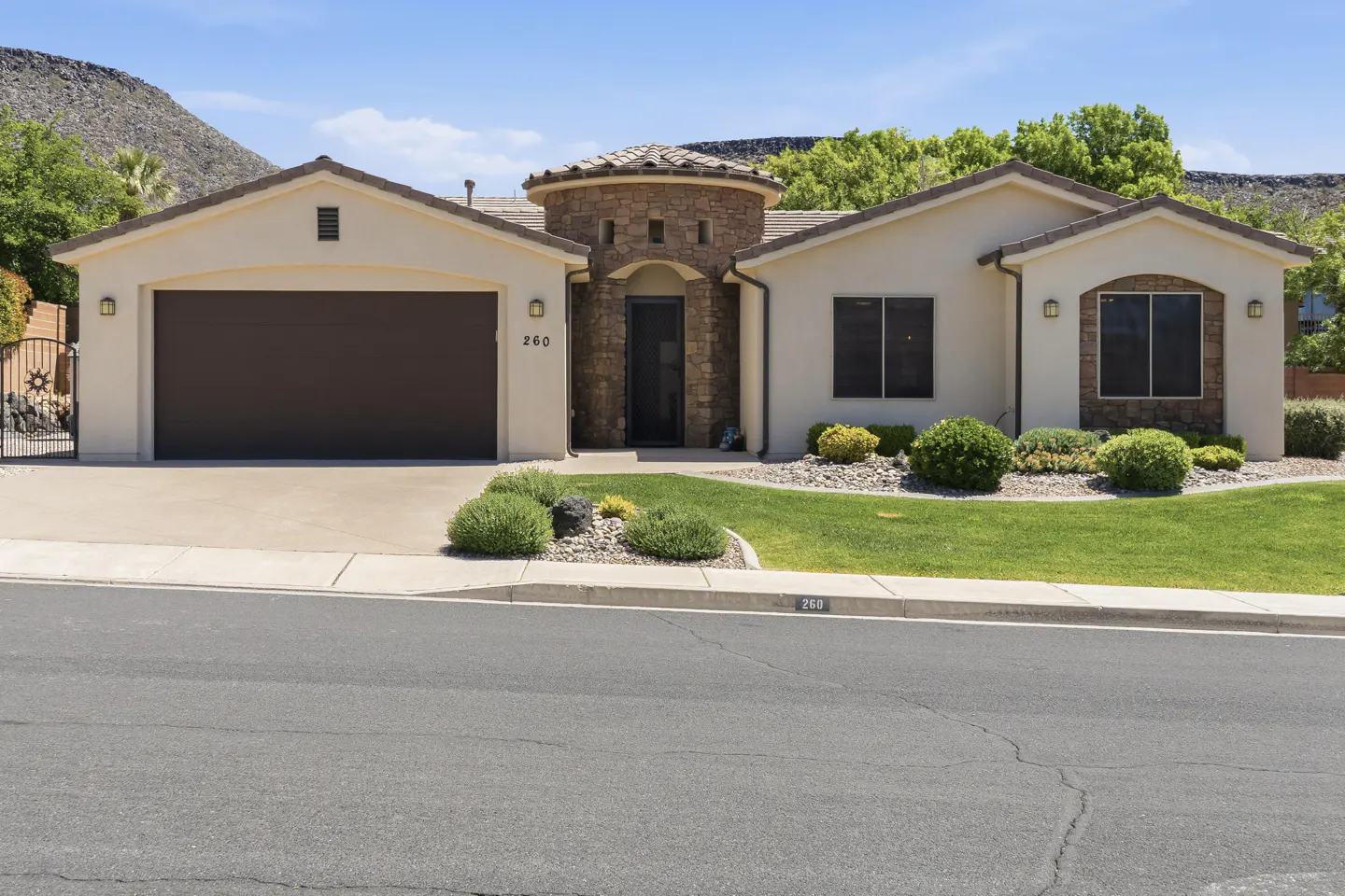 A single-story beige house with a brown garage door and a stone turret entrance.