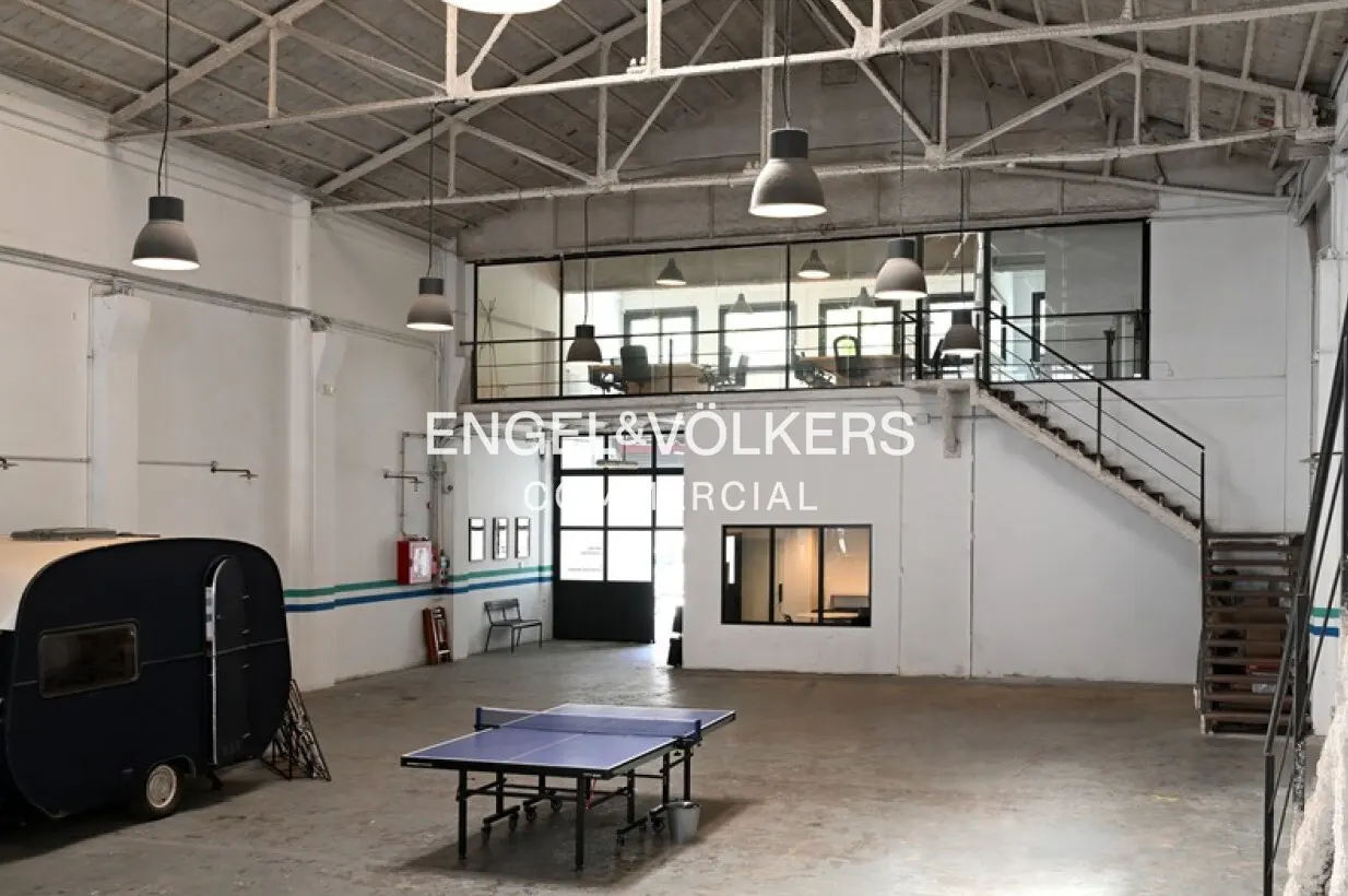 Spacious industrial office with white walls, concrete floors, a blue ping pong table, a vintage camper, and a loft area.