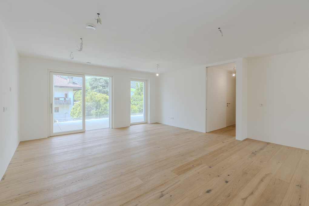 Empty, bright room with light wood floors, white walls, and large glass doors leading to a balcony with mountain views.