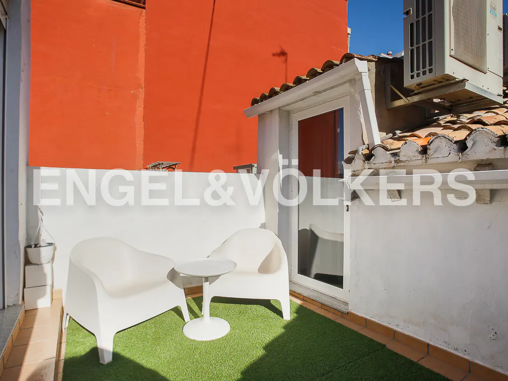 Balcony with white chairs and table on green turf. Orange wall in background. Engel & Volkers logo overlay.