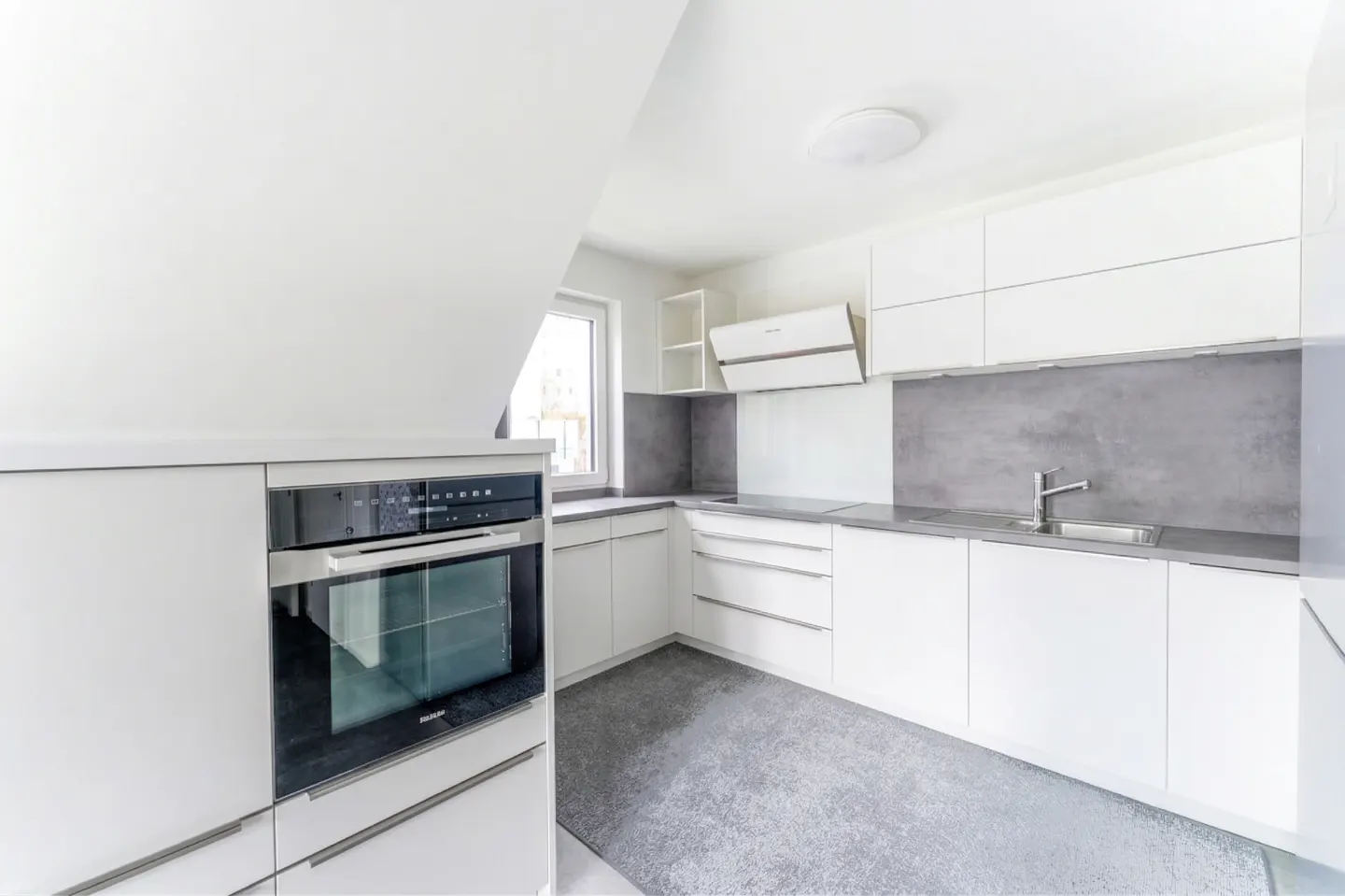 A modern kitchen with white cabinets, gray countertops and backsplash, and stainless steel appliances.