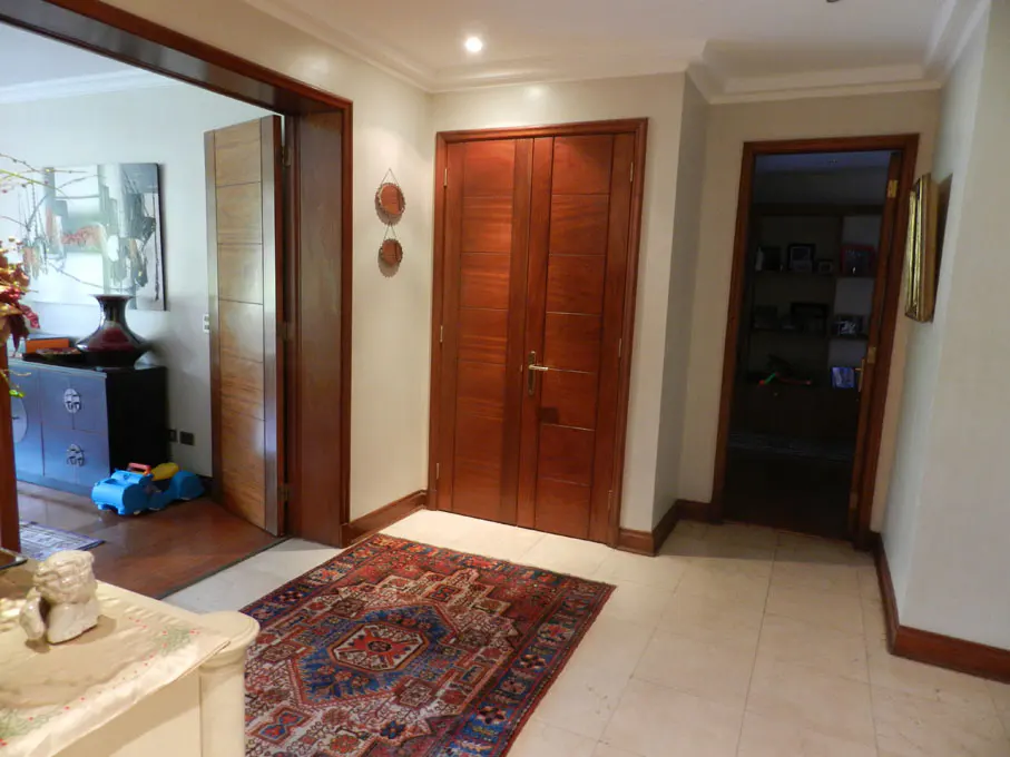 Hallway with beige tile floor, a red and blue rug, and three wooden doorways. Two round mirrors hang on the wall.