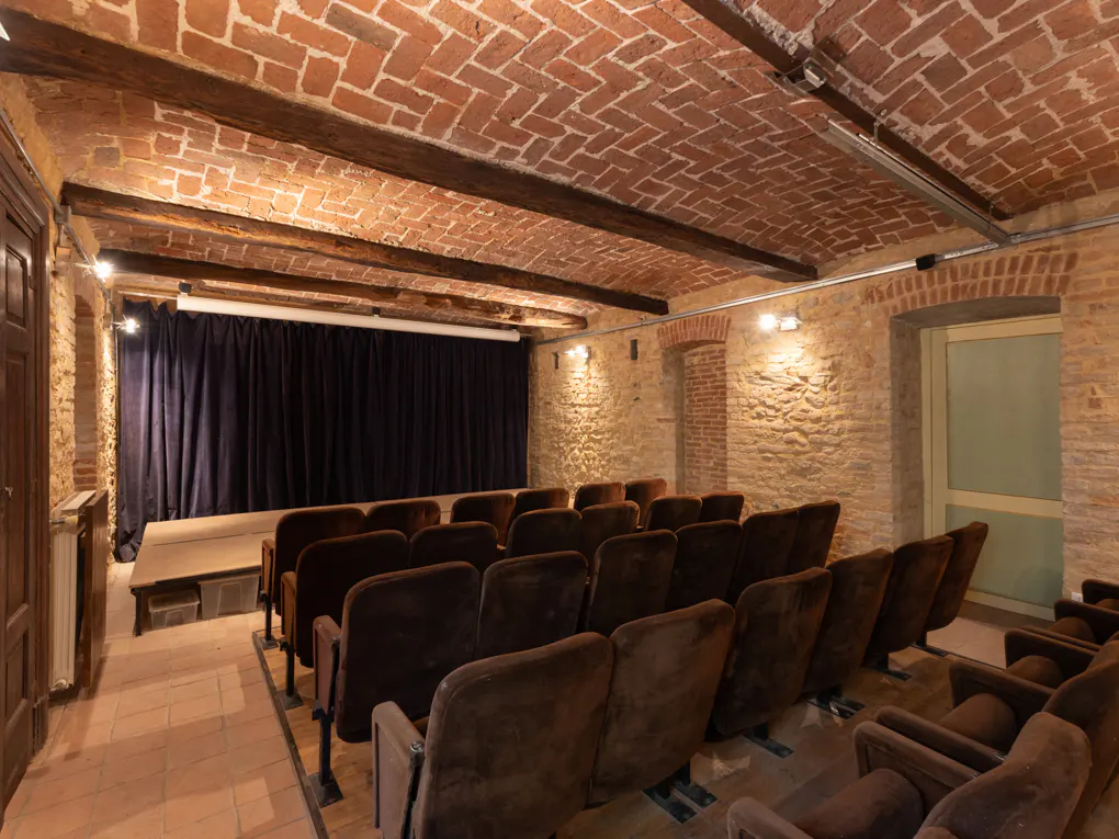 Interior of a small theater with brown velvet seats, brick walls, and a stage with a black curtain.