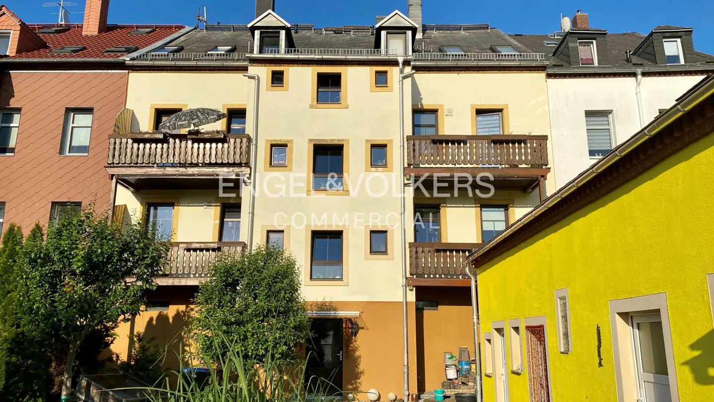 Exterior view of a multi-story building with balconies and various window sizes, next to a bright yellow building.
