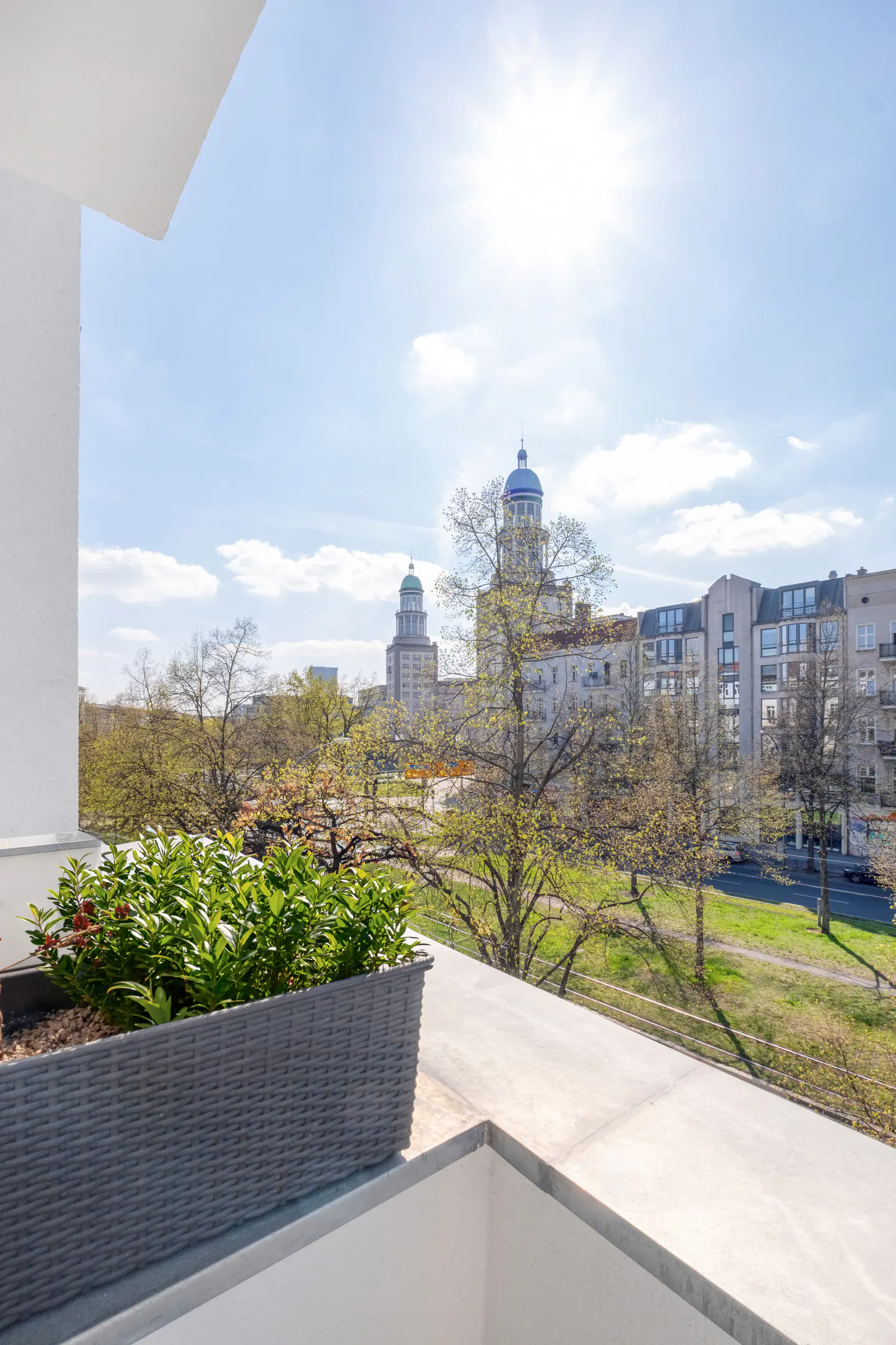 Balcony view of Berlin cityscape. A gray planter box with green plants sits on the balcony. Buildings and trees are in the background.