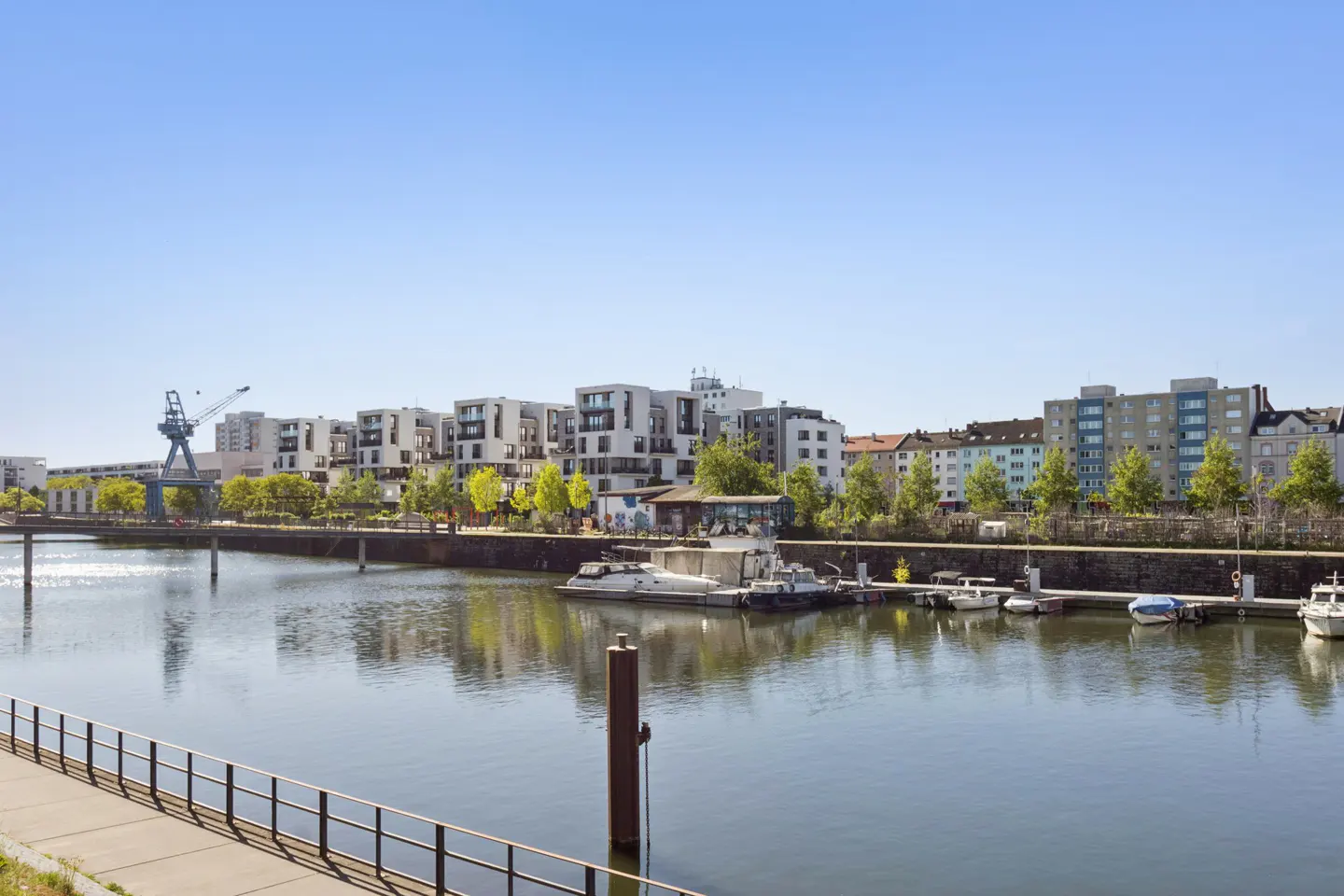 Waterfront view of modern apartments and boats docked along a canal under a clear blue sky.