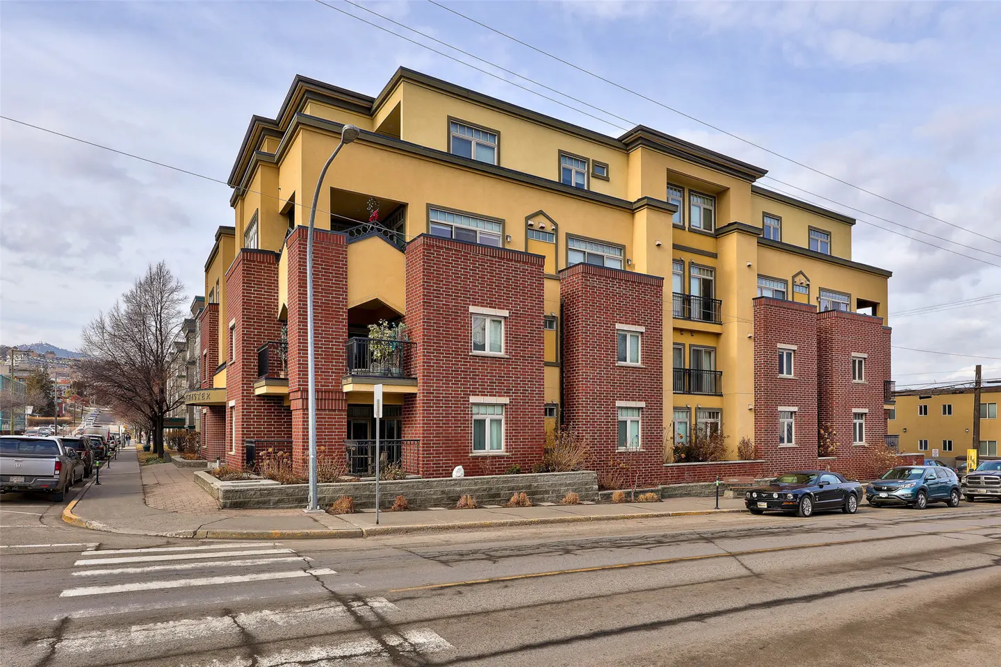 A four-story yellow apartment building with brick accents on a city street with parked cars.