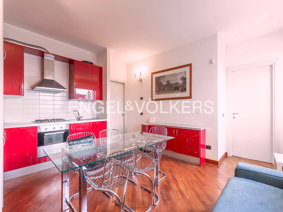 Bright kitchen and dining area with red cabinets, stainless steel appliances, glass table, and wire chairs on a wood floor.