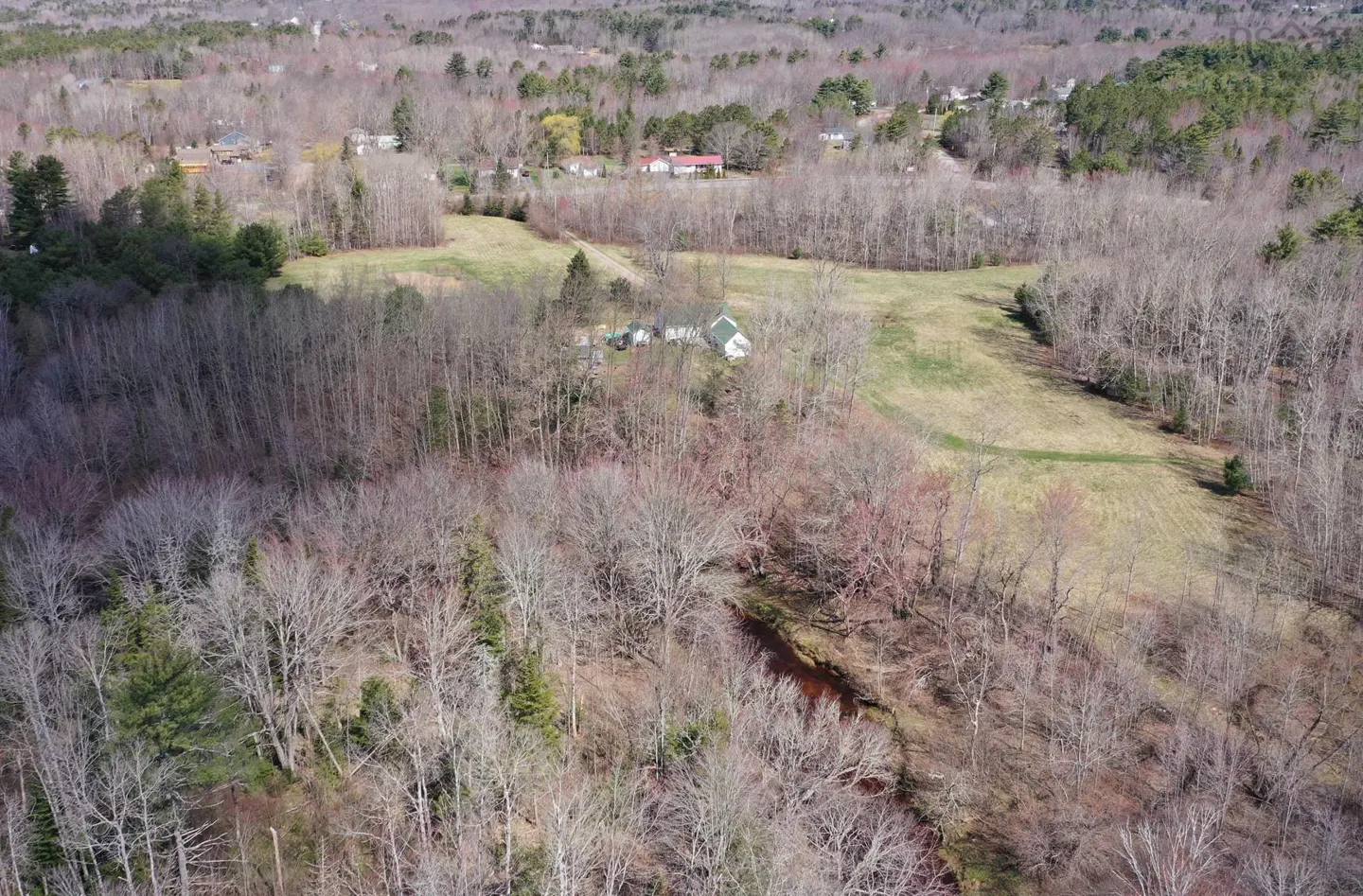Aerial view of a rural landscape with a small house, fields, and a stream surrounded by bare trees.