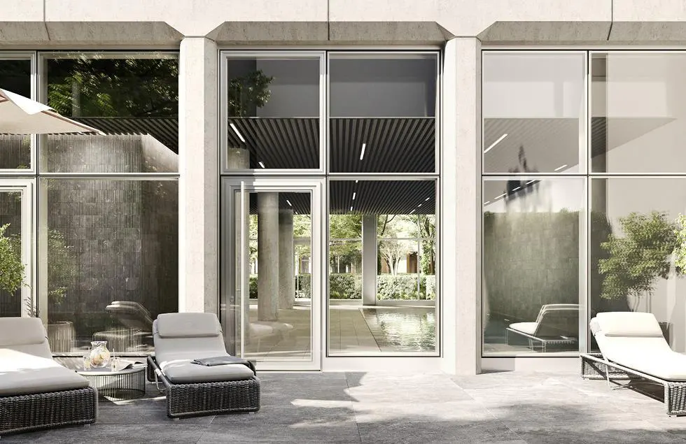 Patio with lounge chairs outside a modern building with large windows. A pool is visible through the open doorway.