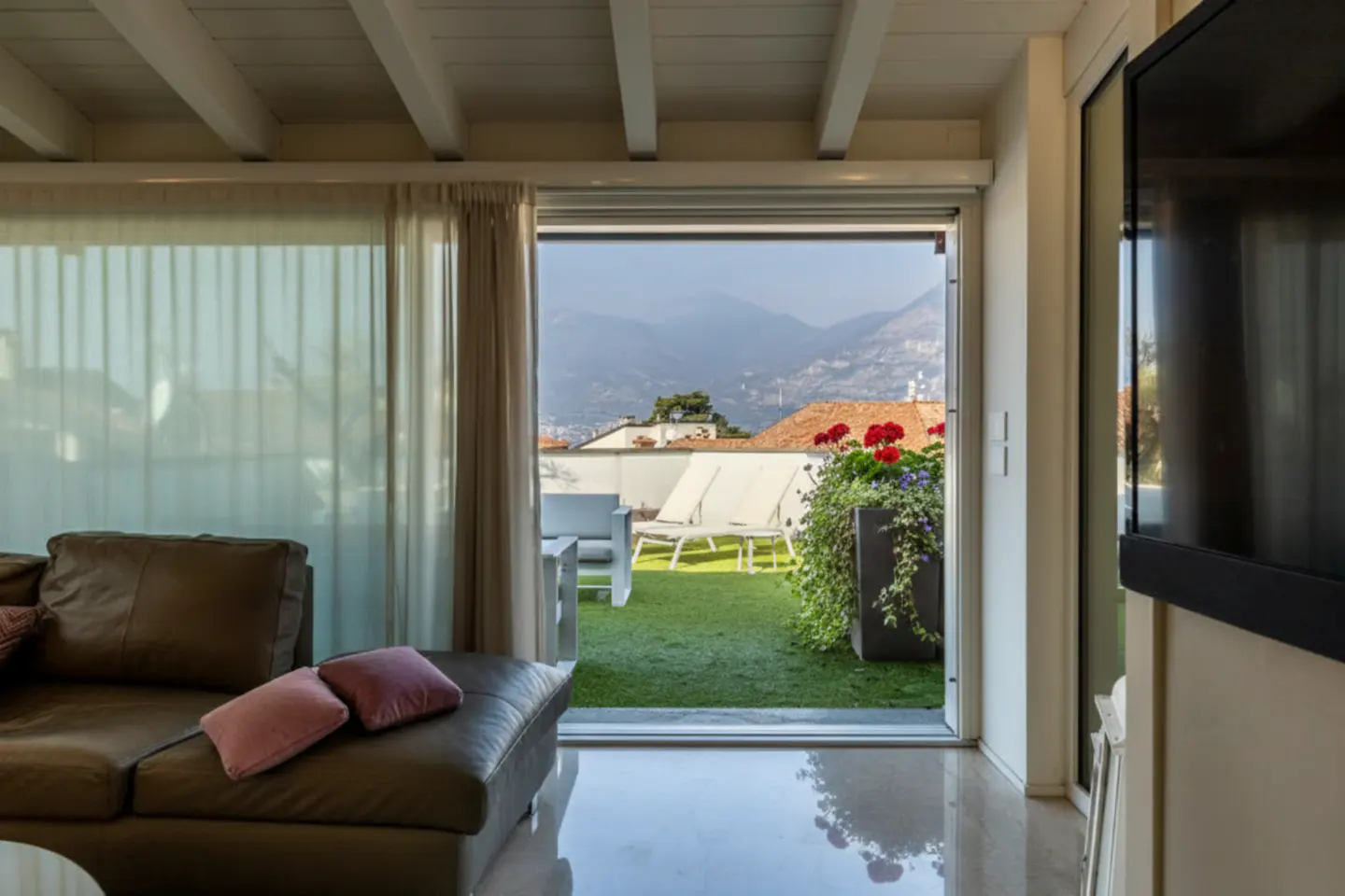 Living room with brown leather couch, pink pillows, and sliding glass doors to a rooftop patio with mountain views.