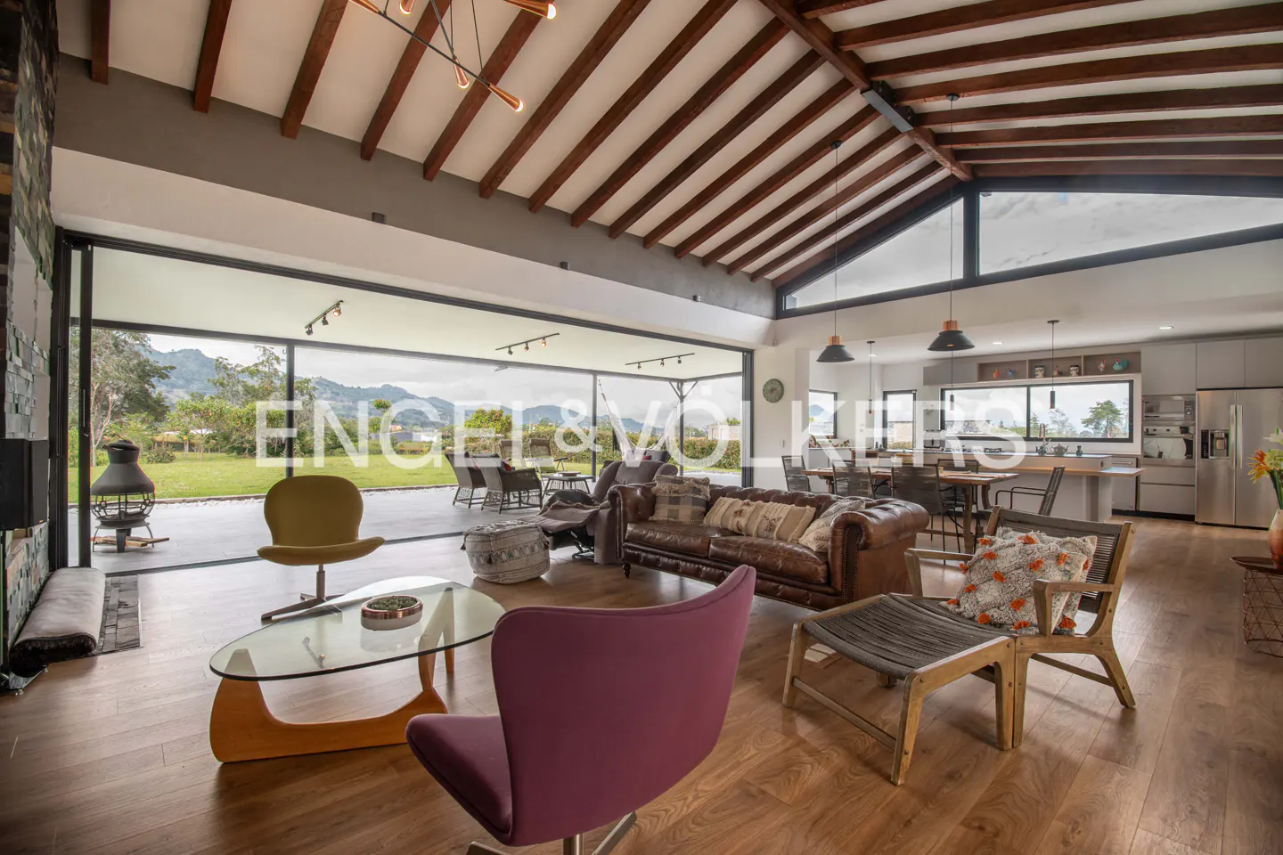 Open-concept living room with wood floors, exposed beams, and floor-to-ceiling windows overlooking a green lawn.