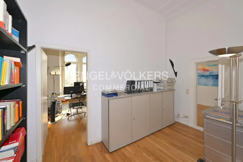Office space with wood floors, white walls, and open doorways. A bookcase, cabinets, and office equipment are visible.