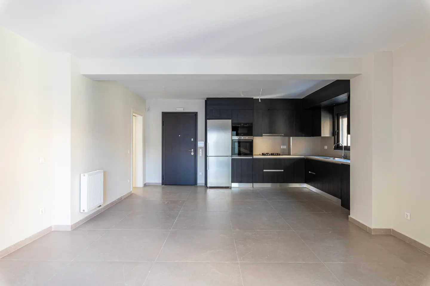 An open-concept apartment with a dark wood kitchen, stainless steel appliances, and light gray tile flooring.