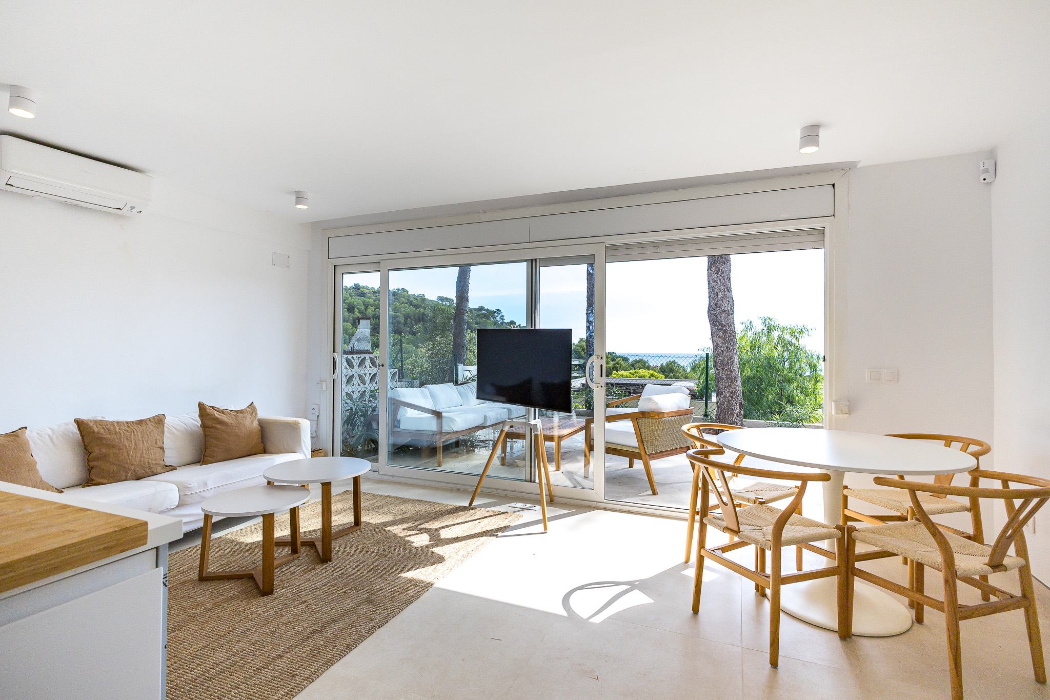 Bright living room with white sofa, two coffee tables, dining area, and large sliding doors opening to a scenic patio. [AI-generated text]
