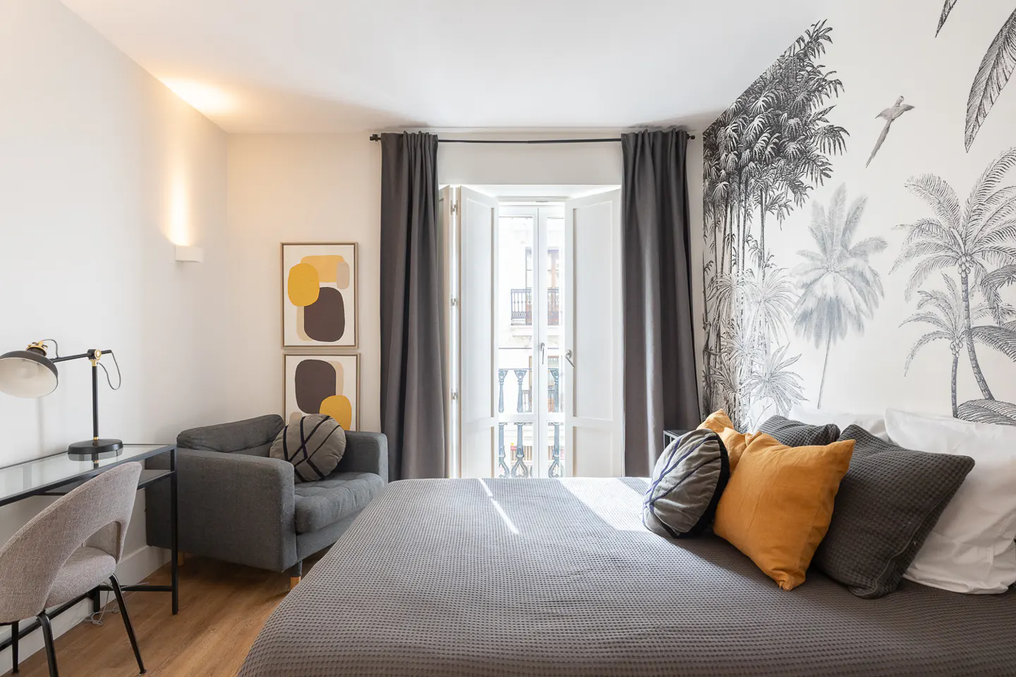 Bedroom with gray bedspread, pillows, and tropical wallpaper. Desk, chair, and gray loveseat are also visible.