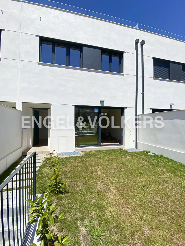 Exterior view of a modern, white townhouse with a green lawn and black framed windows. The Engel & Völkers logo is visible on the building.