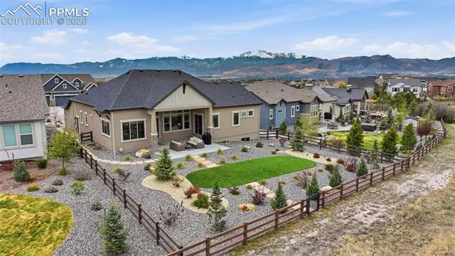 Aerial view of a beige house with a dark roof, a fenced backyard with gravel, and mountains in the background.