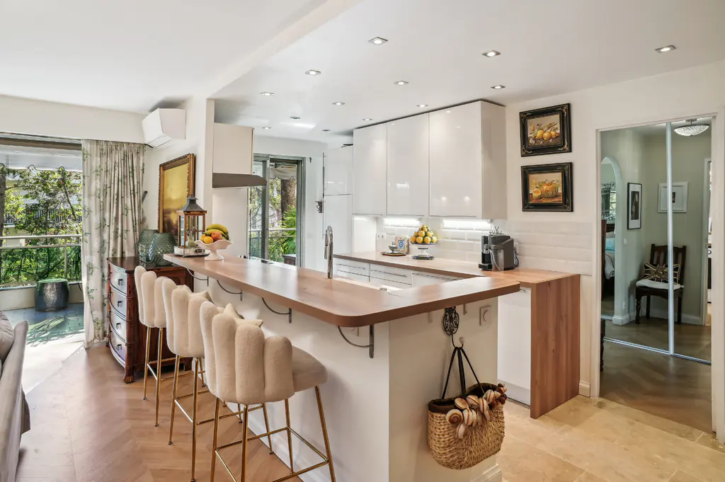Bright kitchen with white cabinets, wood countertops, and beige bar stools. Balcony with greenery visible through sliding glass doors.