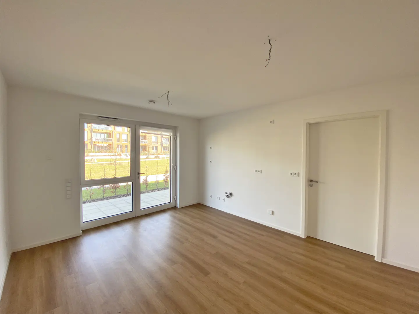 Empty room with wood floor, white walls, and a glass door to the outside. A white door is on the right.