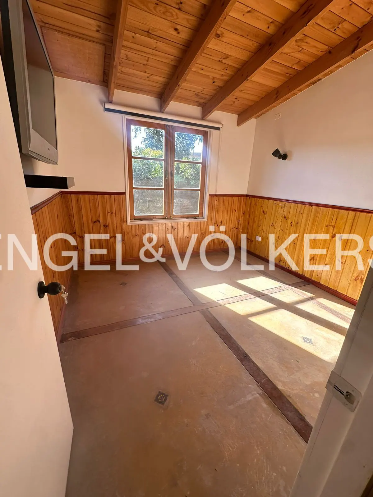 Empty room with wood paneling, ceiling, and floor. A window lets in natural light. Engel & Völkers logo is visible.