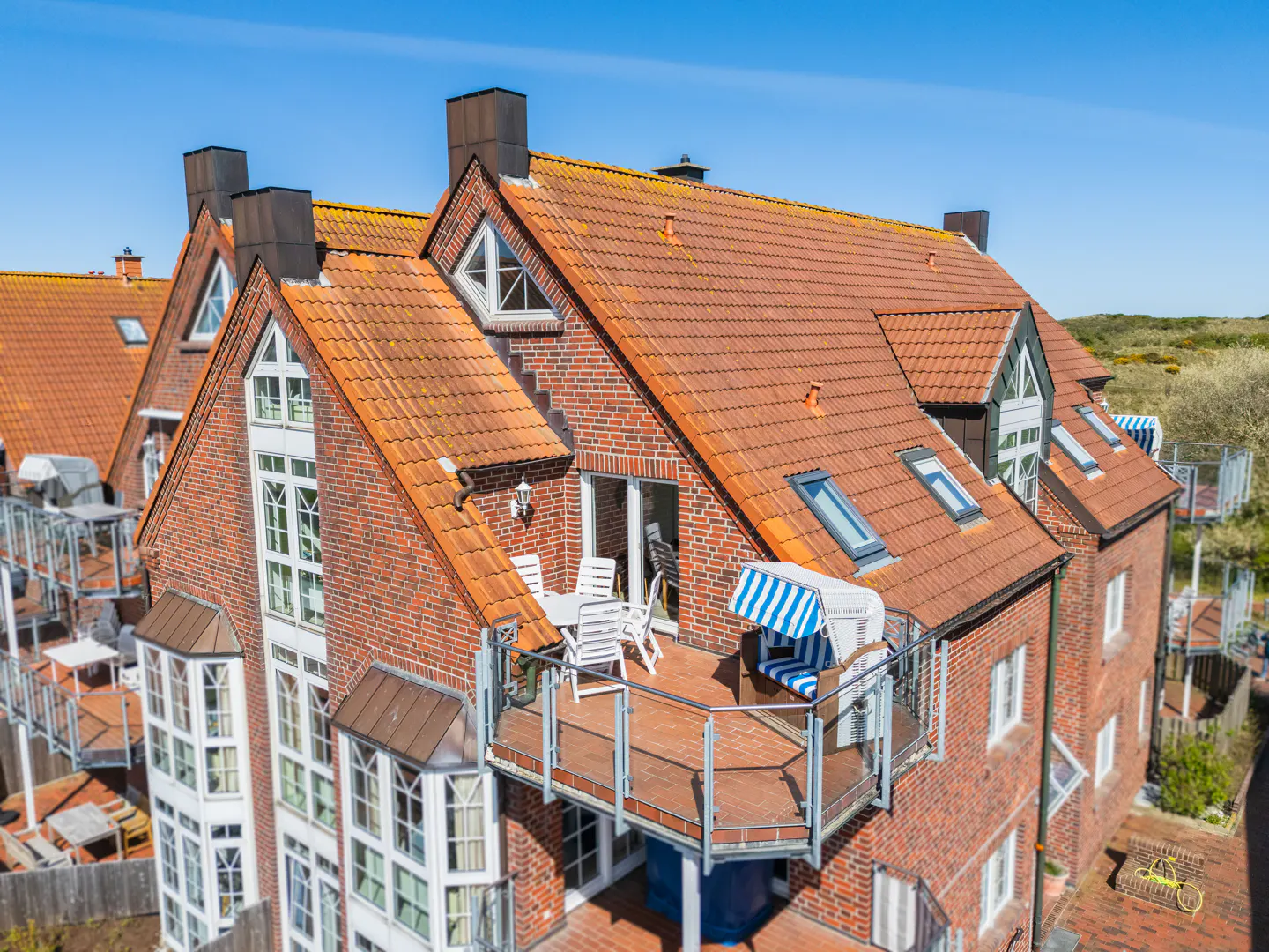 Aerial view of a red brick apartment building with a balcony, white chairs, and a blue and white striped beach chair.