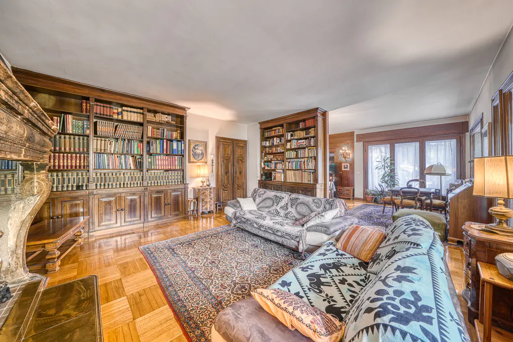 A living room with hardwood floors, two sofas, and two large, dark wood bookshelves filled with books.