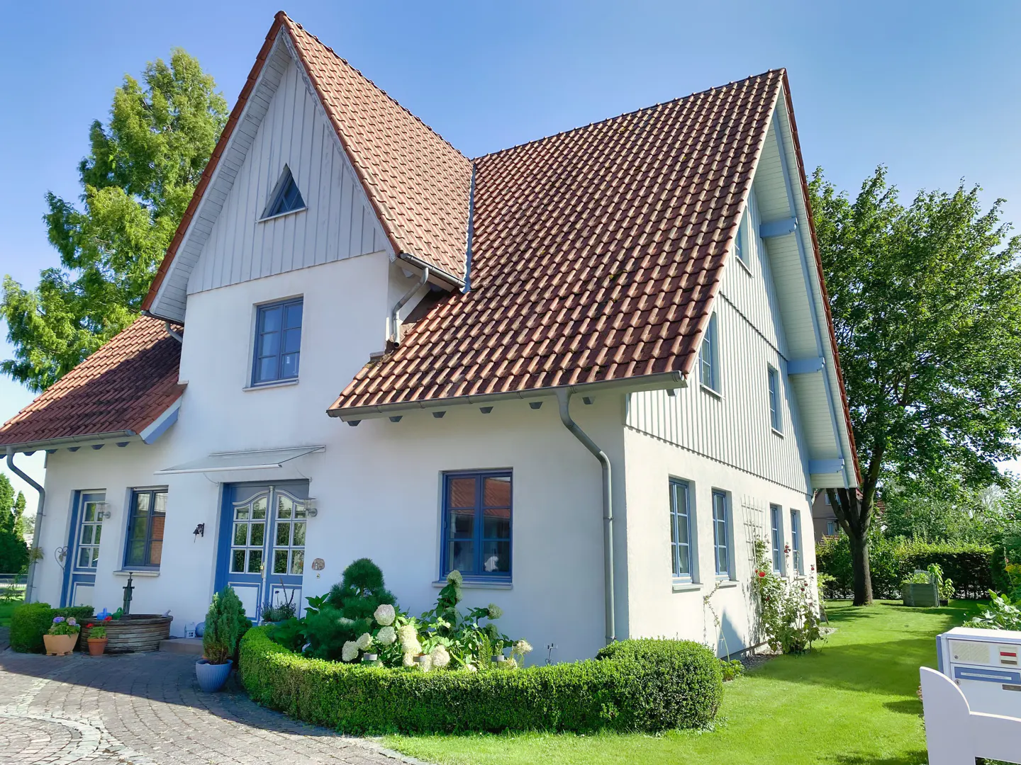 Two-story white house with a red tile roof, blue trim, and a well-manicured lawn.