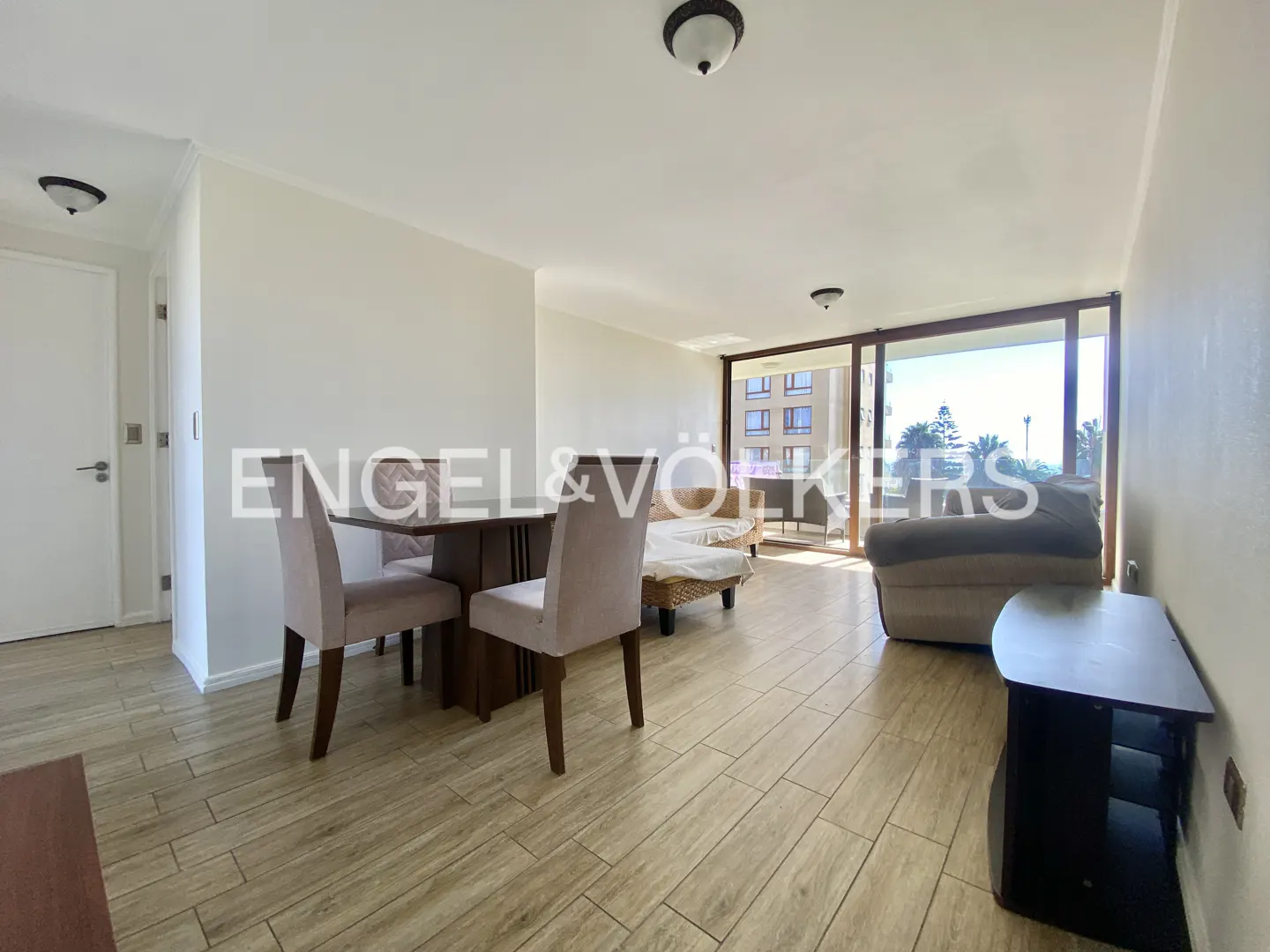 Living room with wood floors, table, chairs, sofa, and sliding glass doors to a balcony with ocean view.
