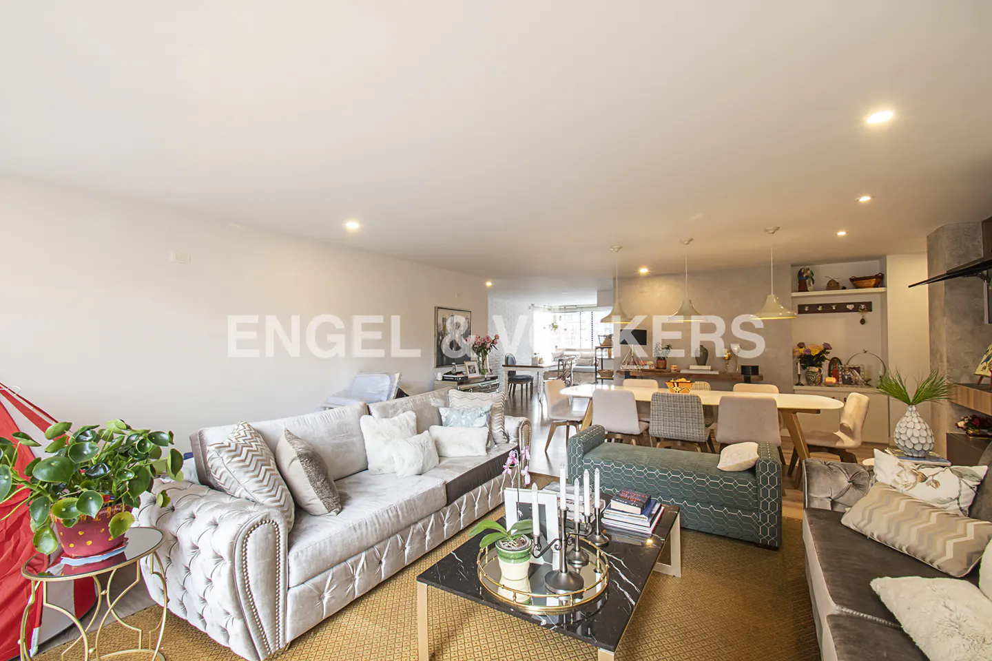 Open-concept living and dining area with a gray sofa, marble coffee table, and a long dining table with chairs.