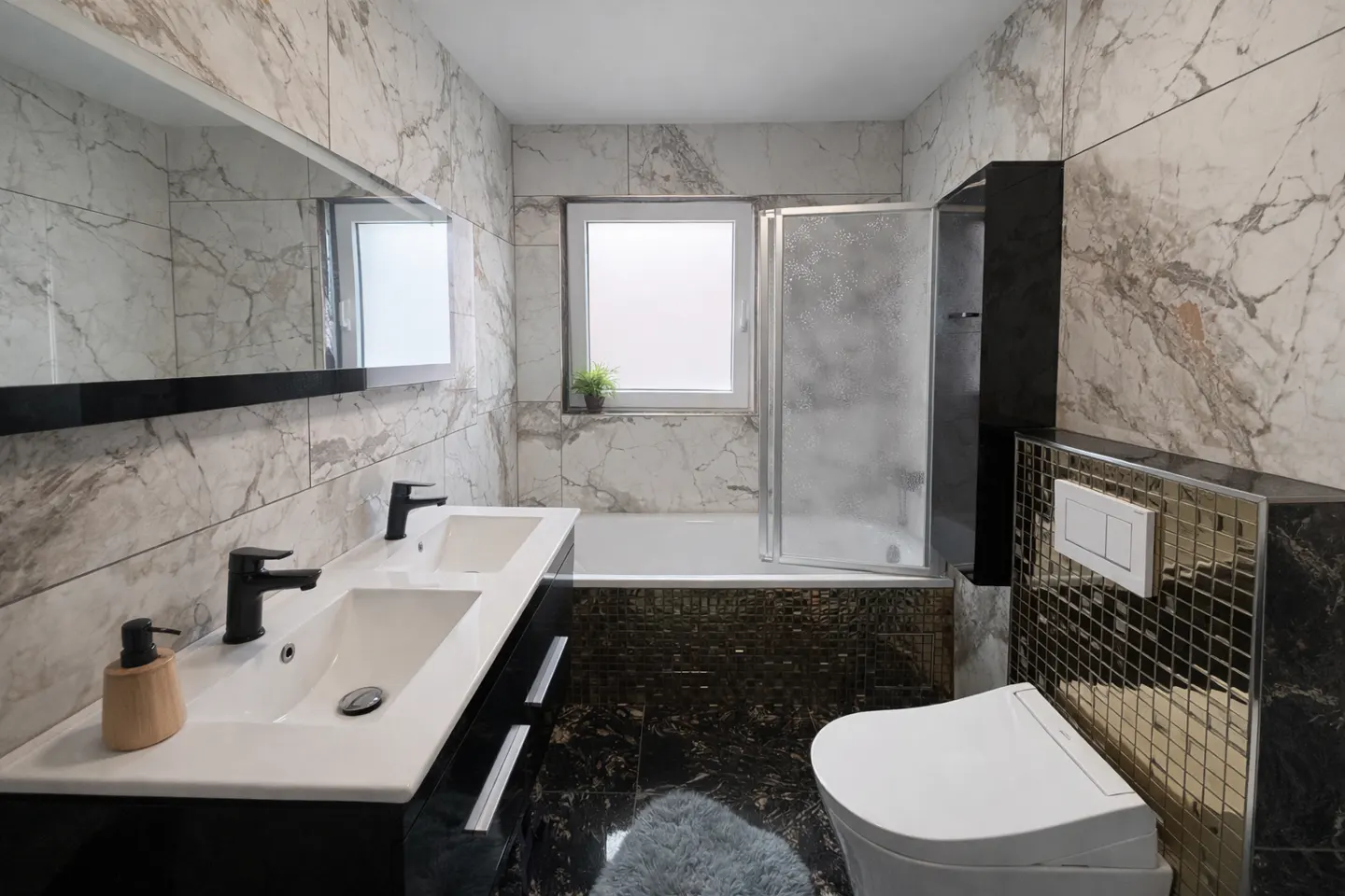 Modern bathroom with marble walls, black vanity with double sinks, black fixtures, toilet with gold mosaic tile accent wall, and glass shower door.