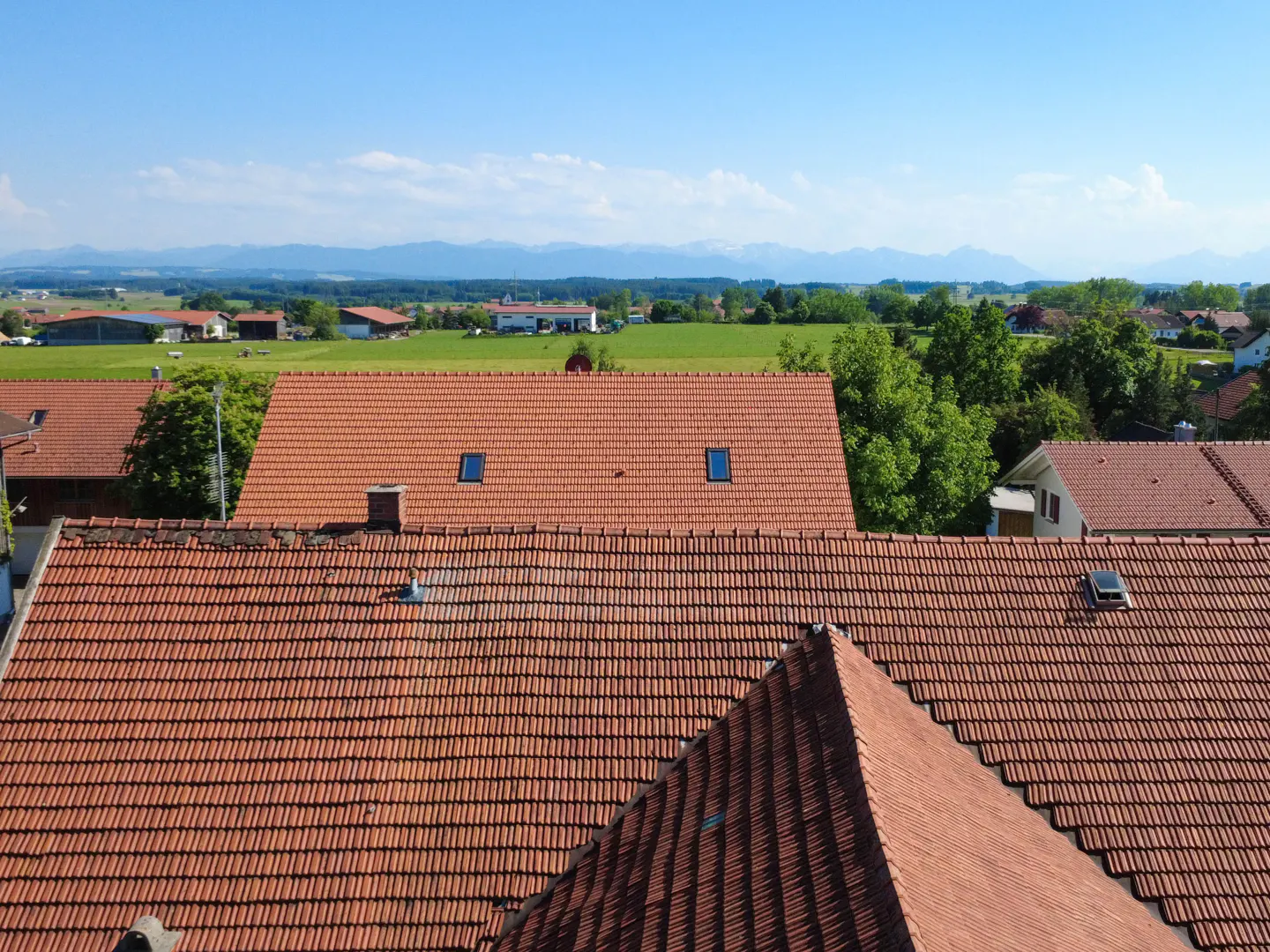 View of red-tiled rooftops, green fields, and distant mountains under a blue sky.