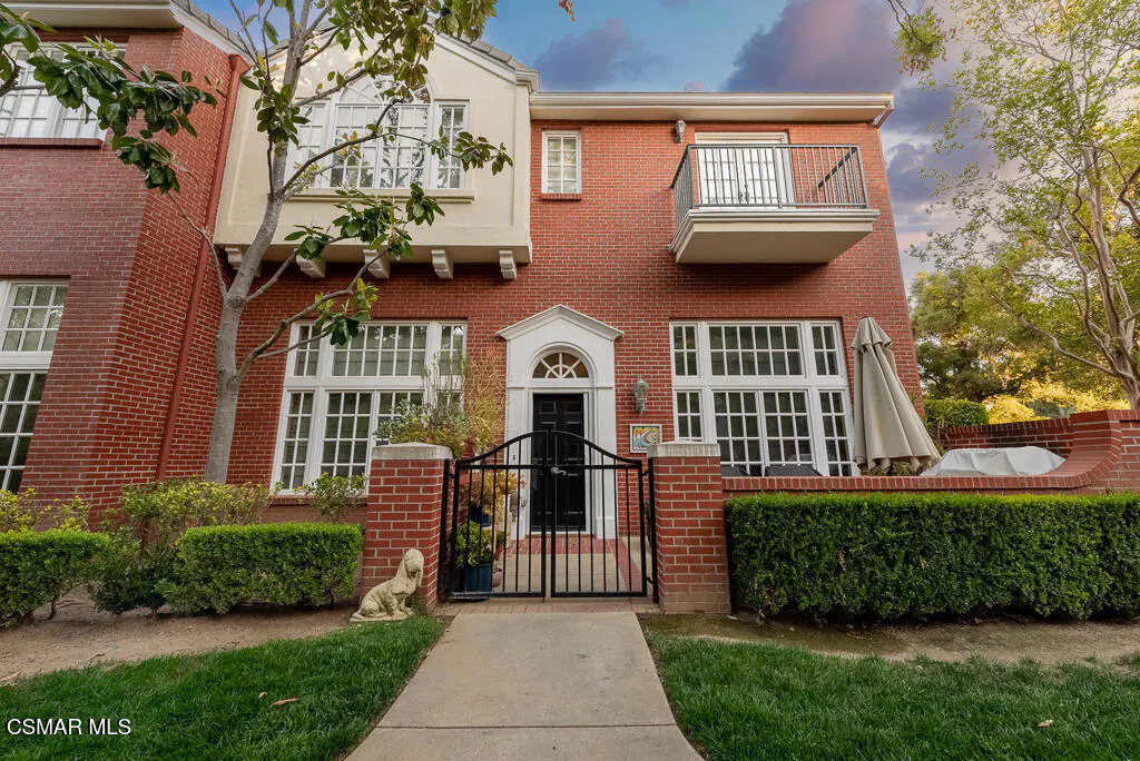 Exterior of a red brick two-story house with a black gate, white windows, and a small balcony.