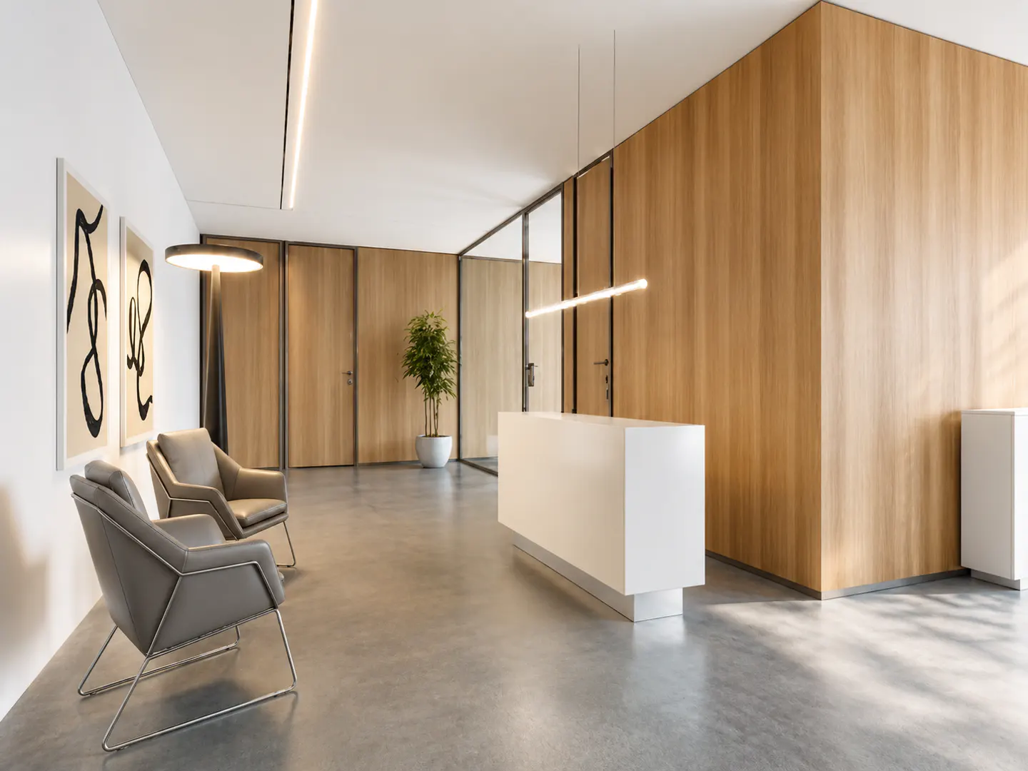 Modern office reception with a white desk, grey armchairs, wood-paneled walls, and abstract art on a white wall.