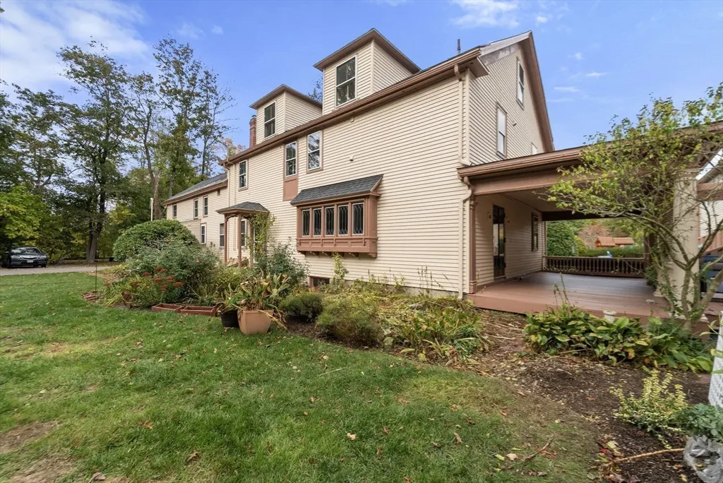 Two-story beige house with brown trim, a bay window, and a covered side porch, set in a yard with trees and landscaping.