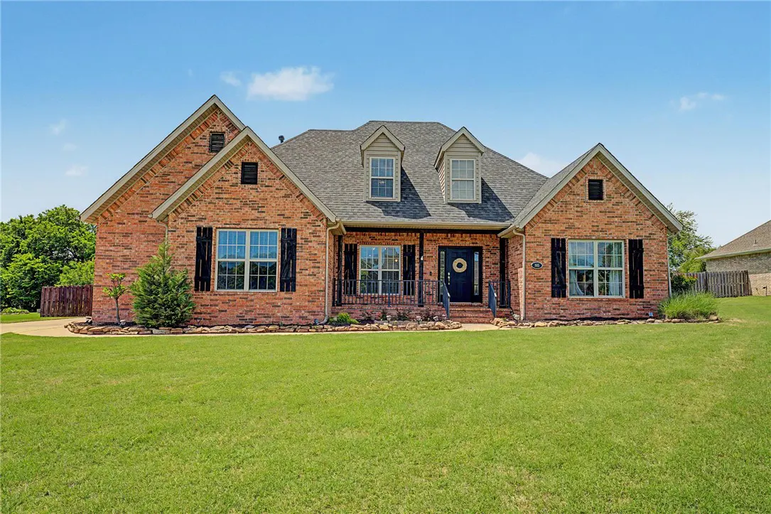 Red brick house with black shutters, a gray roof, and a green lawn under a blue sky.