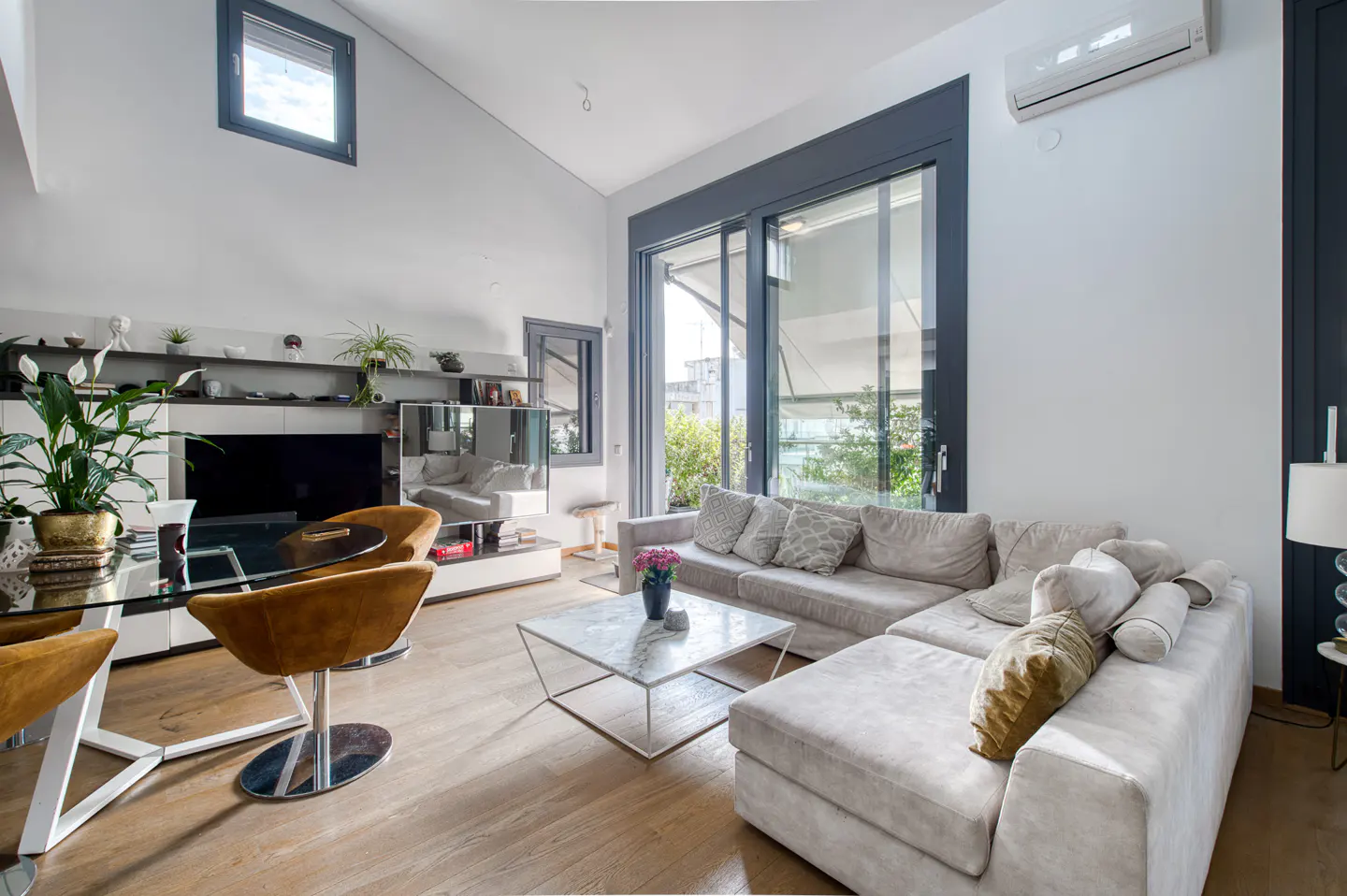 Modern living room with high ceilings, a large beige sectional sofa, marble coffee table, and mustard yellow dining chairs.