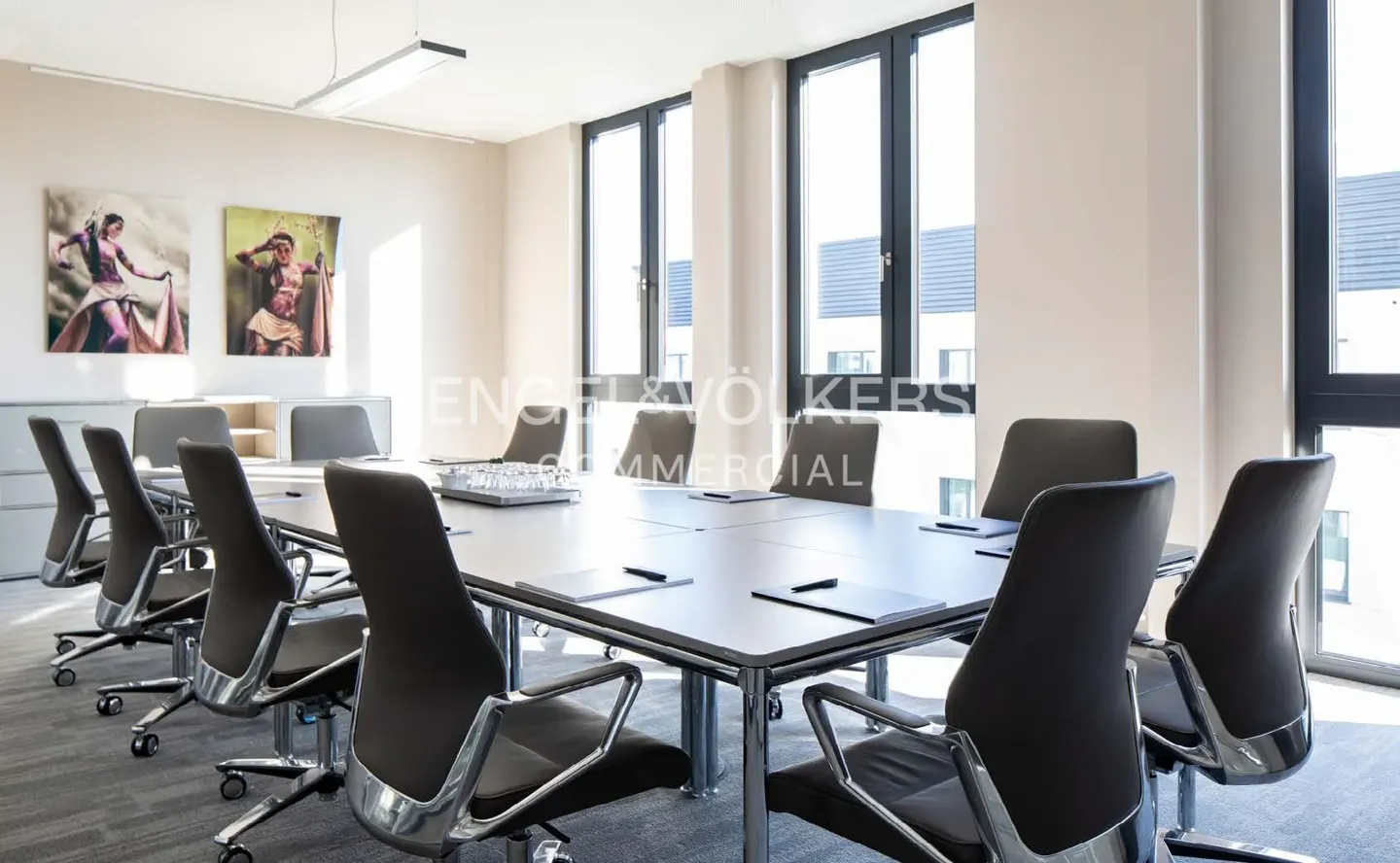 Bright conference room with a long table, black chairs, and large windows. Artwork adorns the walls.