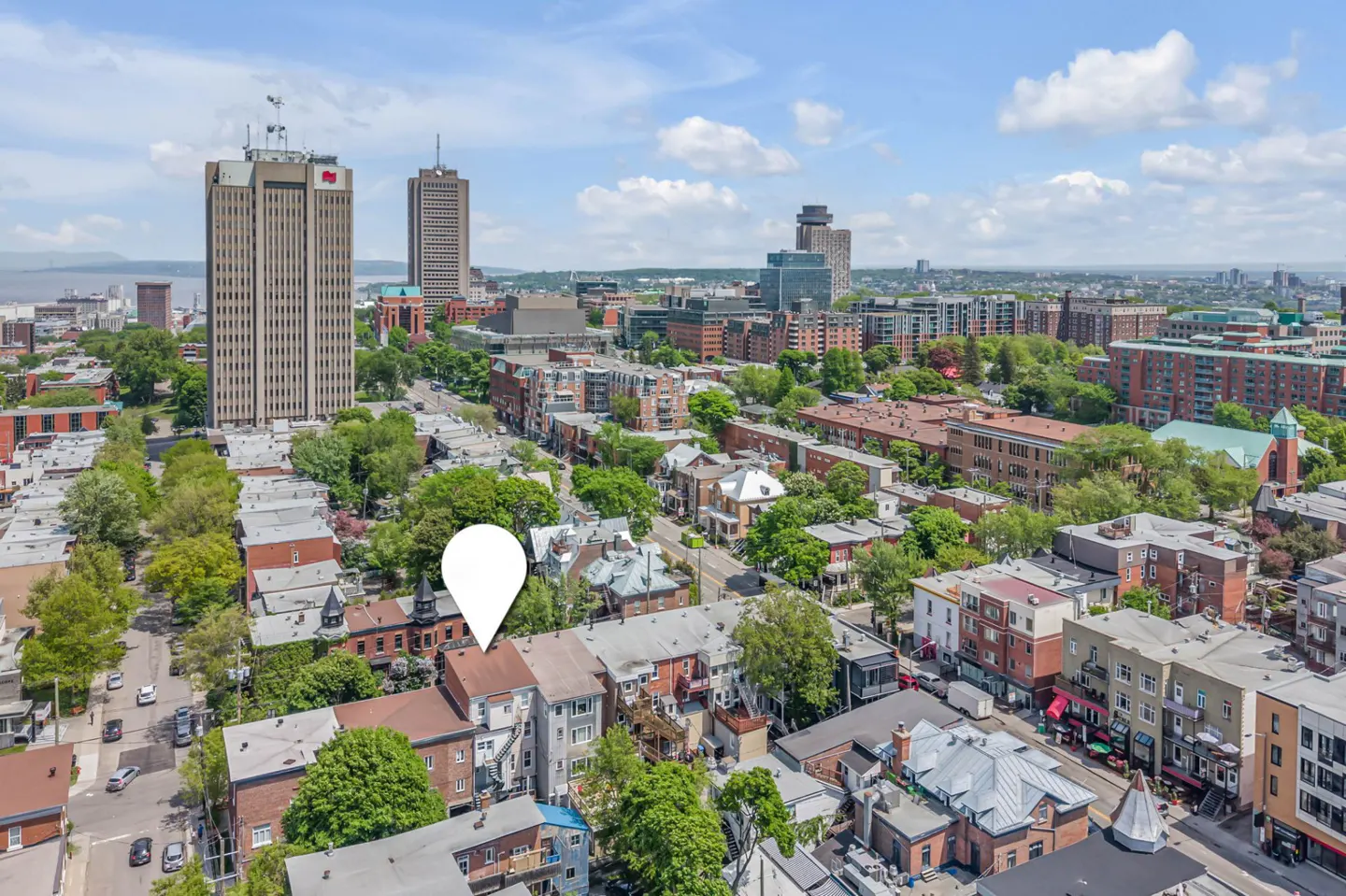 Aerial view of a dense city neighborhood with a white location pin marking a specific building amidst trees and skyscrapers.