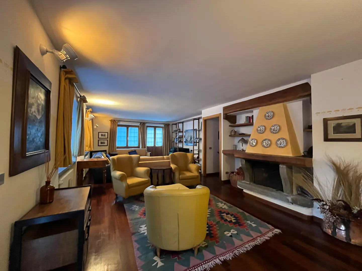 Cozy living room with yellow armchairs, a patterned rug, wooden floors, and a fireplace with decorative plates.