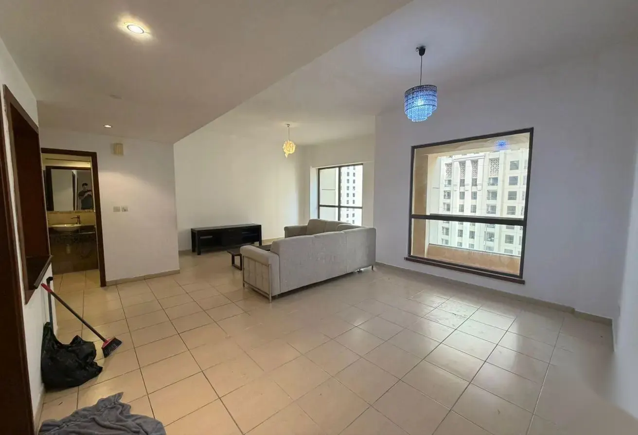 A wide shot of a living room with a gray sofa, TV stand, and tiled floor. A blue chandelier hangs near a window with a city view.