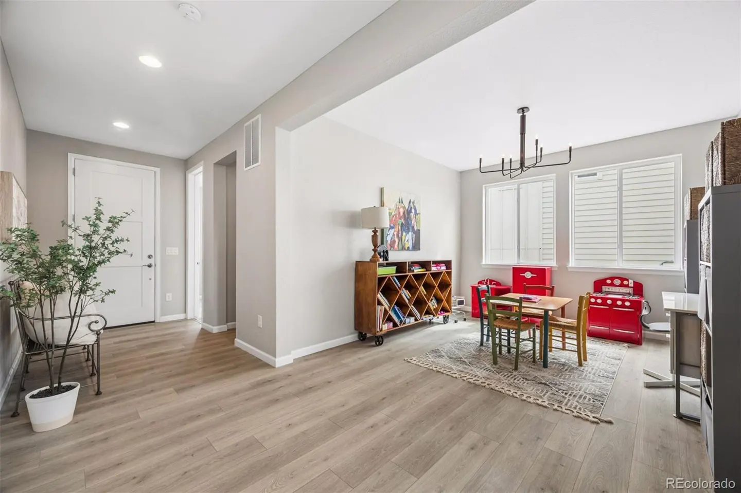 A bright, open-concept room with light wood floors, a white door, and a child's play area with a red toy kitchen set.