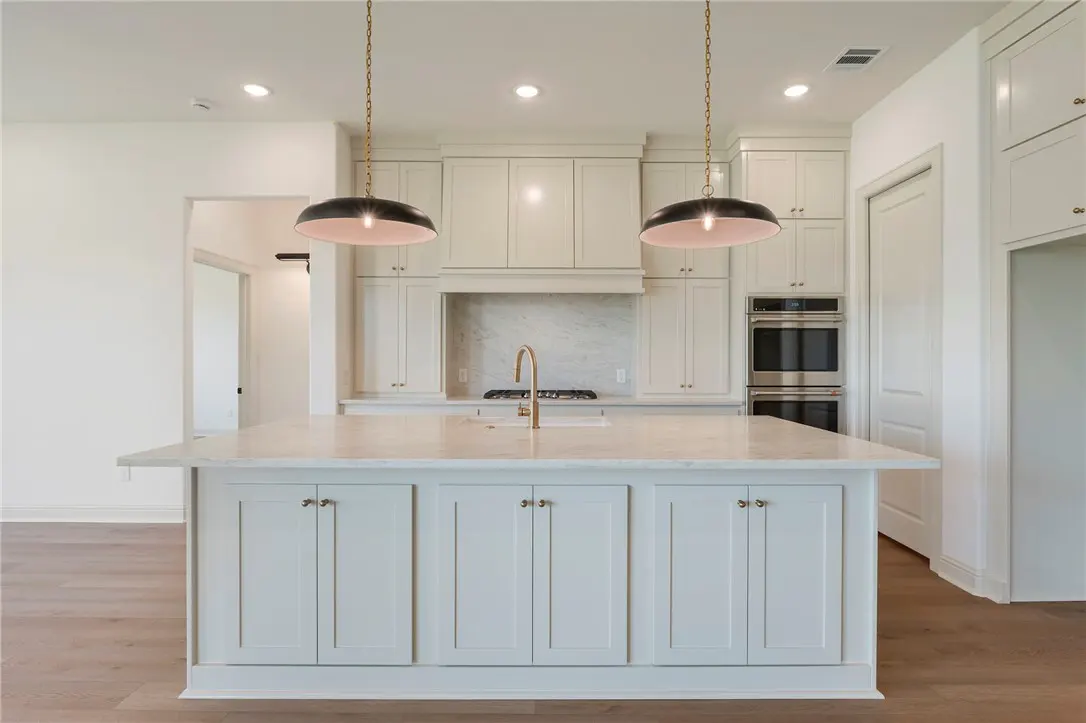 Bright kitchen with white cabinets, marble countertops, and stainless steel appliances. Two pendant lights hang above the island.