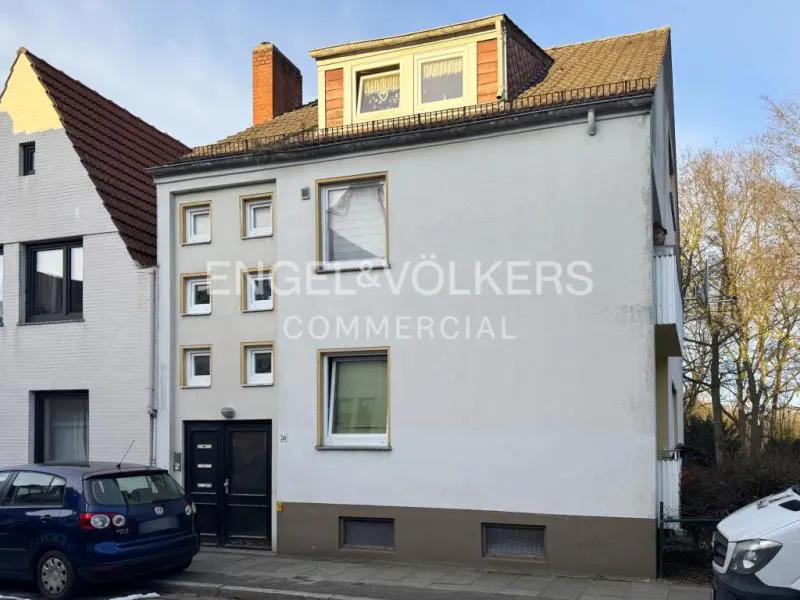 Exterior view of a three-story building with white walls, brown trim, and a dark roof, with Engel & Völkers logo.