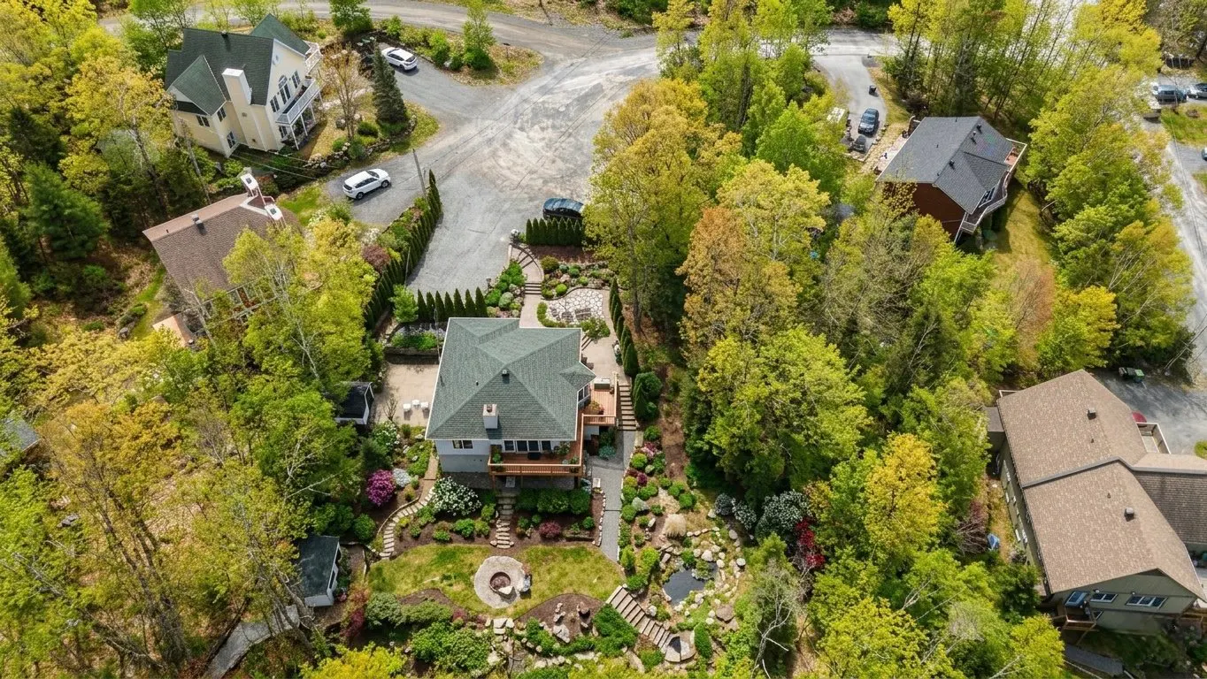 Aerial view of a light gray house with a green roof, surrounded by lush green trees and landscaped gardens.