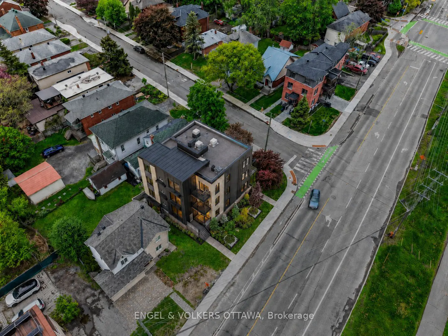 Aerial view of a modern multi-story apartment building surrounded by residential houses and a wide city street.