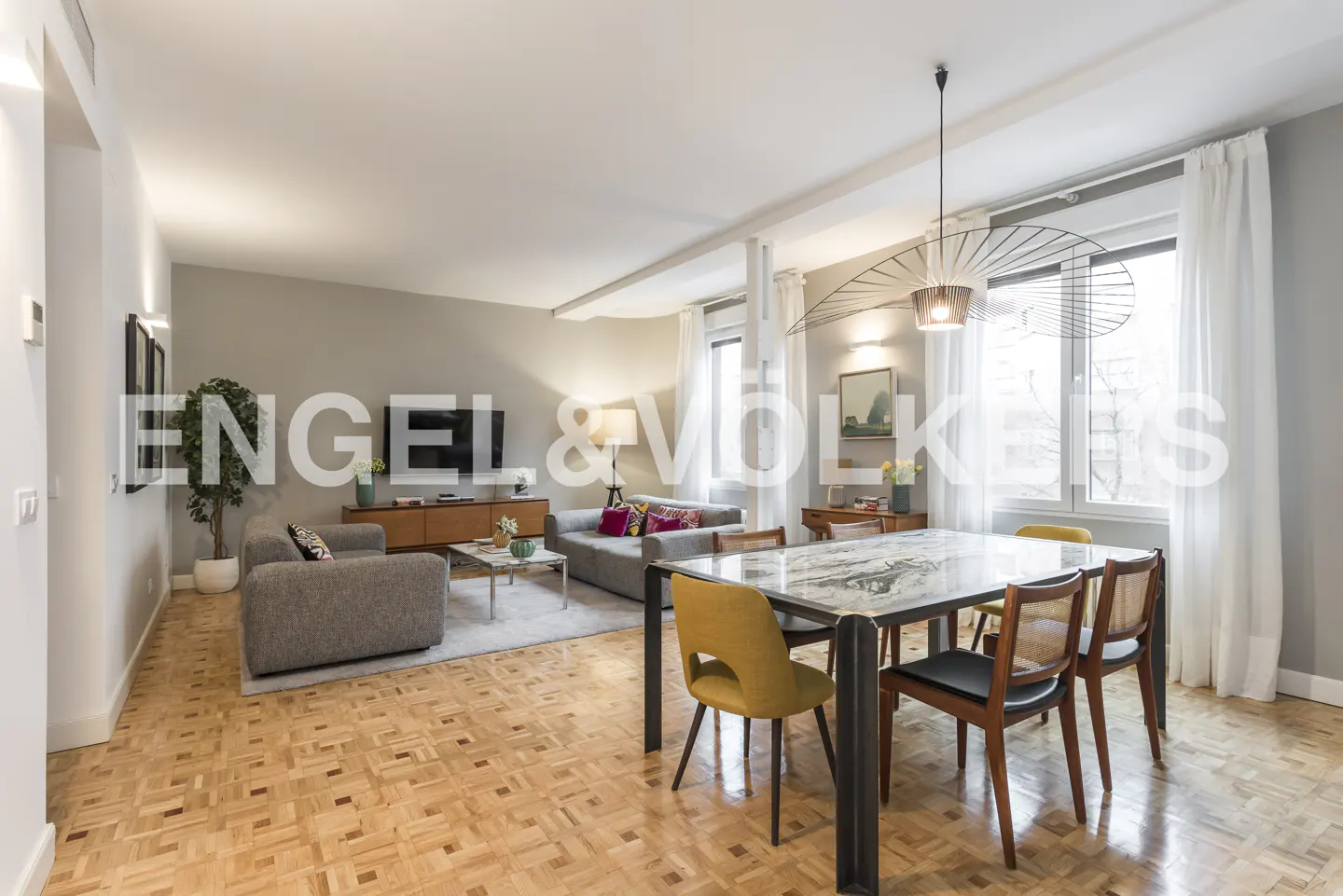 Modern living room with parquet floors, gray sofa, marble dining table, yellow and wooden chairs, and a unique pendant light.