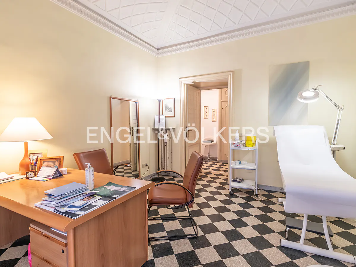 A doctor's office with a wooden desk, brown chairs, and a white examination table on a black and white checkered floor.